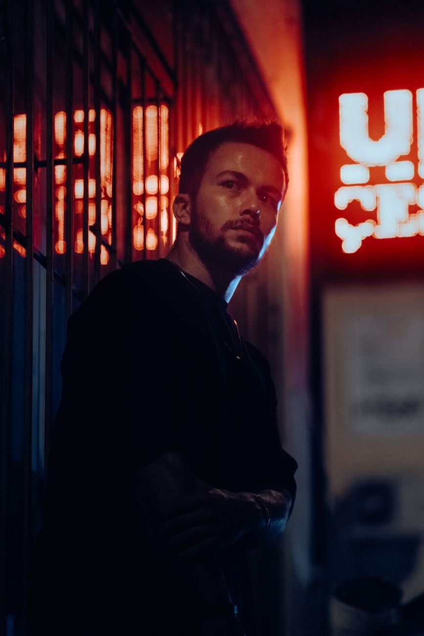 Moody night portrait of a man in a neon-lit alleyway, showcasing urban fashion and style.